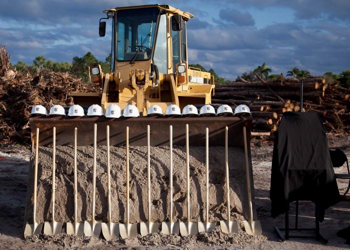 Standing gold shovels with hard hats above them in front of a tractor